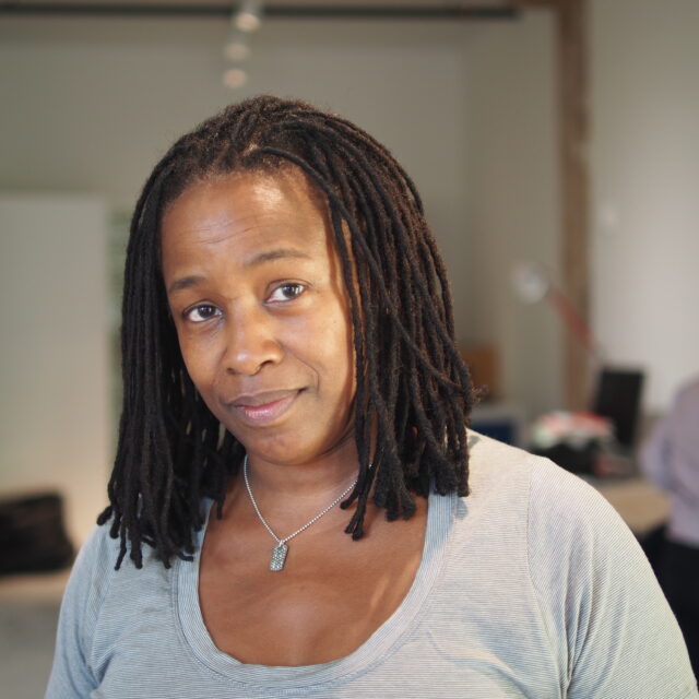 a photo portrait of a Black woman with shoulder-length locs smiling at the camera
