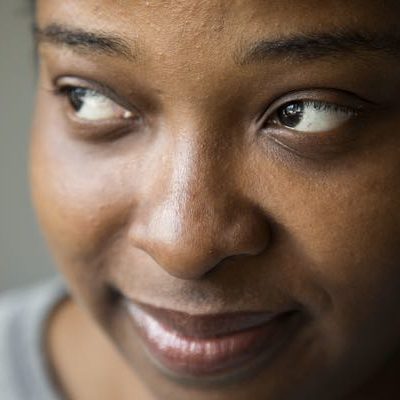 A close up image of young black woman with brown skin, brown eyes looks off camera. She is wearing a gray sweater.