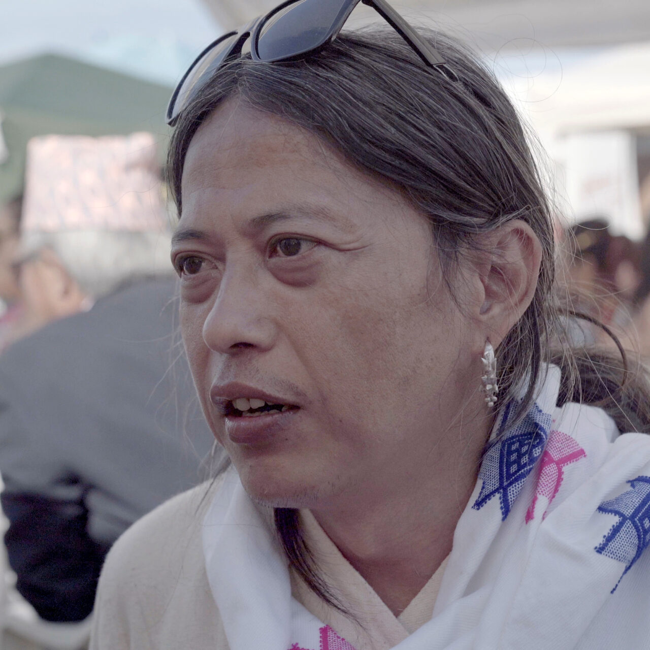 An indigenous Yakthung person with long hair, silver earrings, traditional white scarf with blue and pink star patterns.