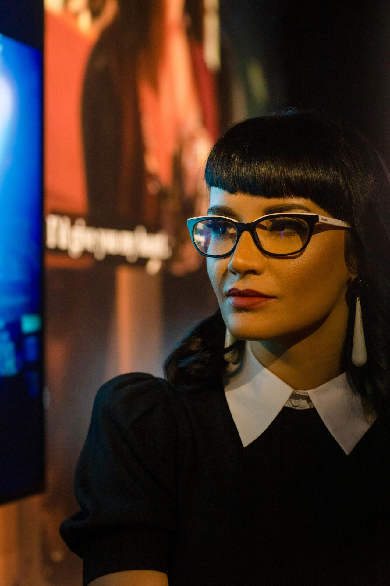 Mashinka Firunts Hakopian is a light-skinned SWANA/Armenian woman with straight, jet-black hair and wears red lipstick and cat-eye framed glasses.