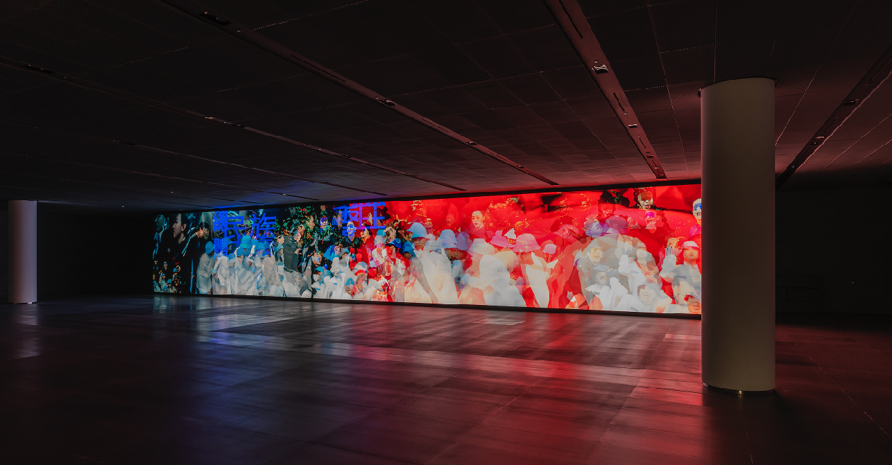 At the Hyundai Vision Hall, there is a dark screen room with a 24-meter-wide hi-resolution display. On the screen is Su’s work, the moment that the photographs captures in the video installation, rich reds and blues interspersed with ghostly images of a crowd.