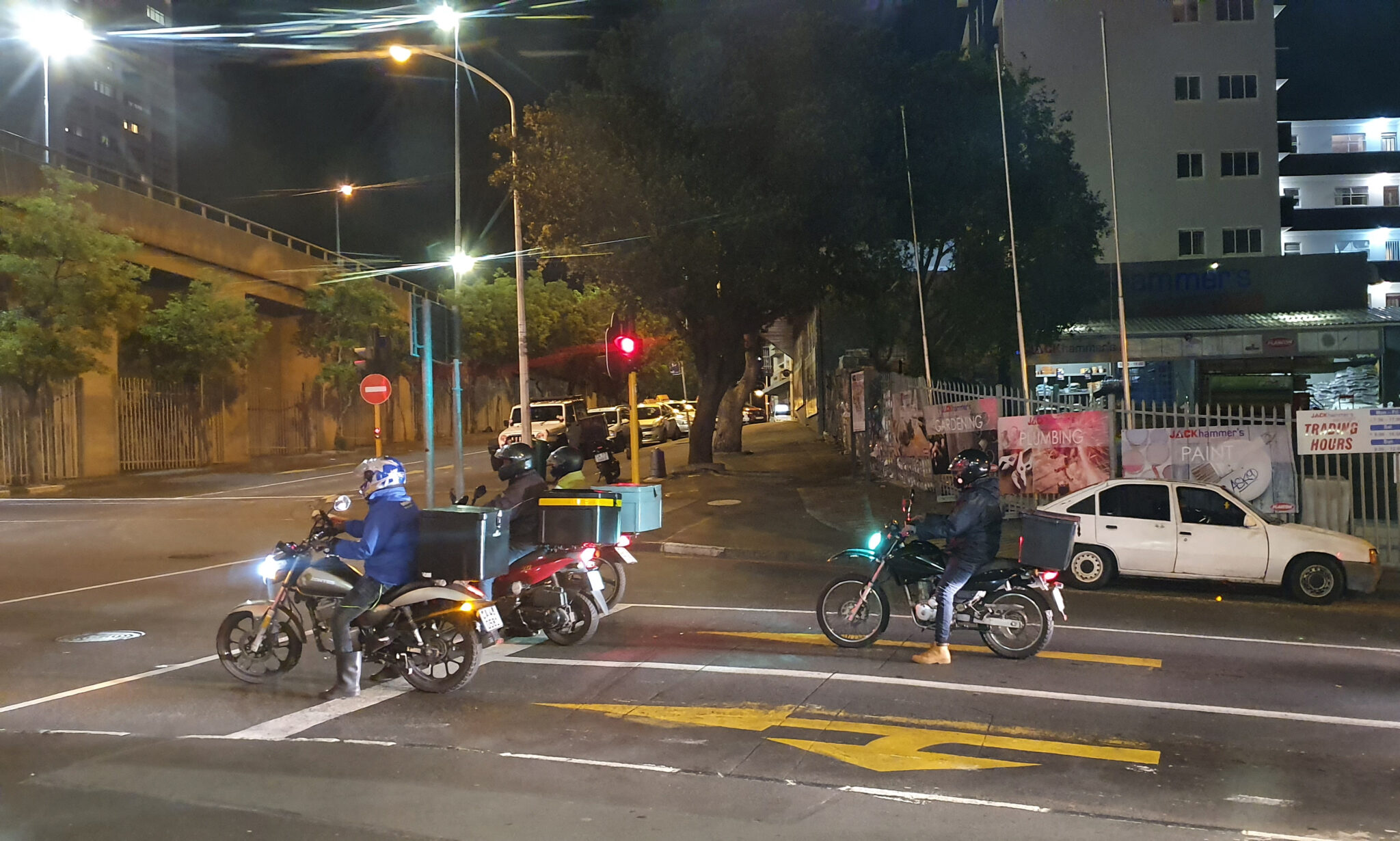Motorcycle couriers, at night, are waiting at the intersection of stop light, Buitenkant Street and Mill Streets in Cape Town, South Africa.
