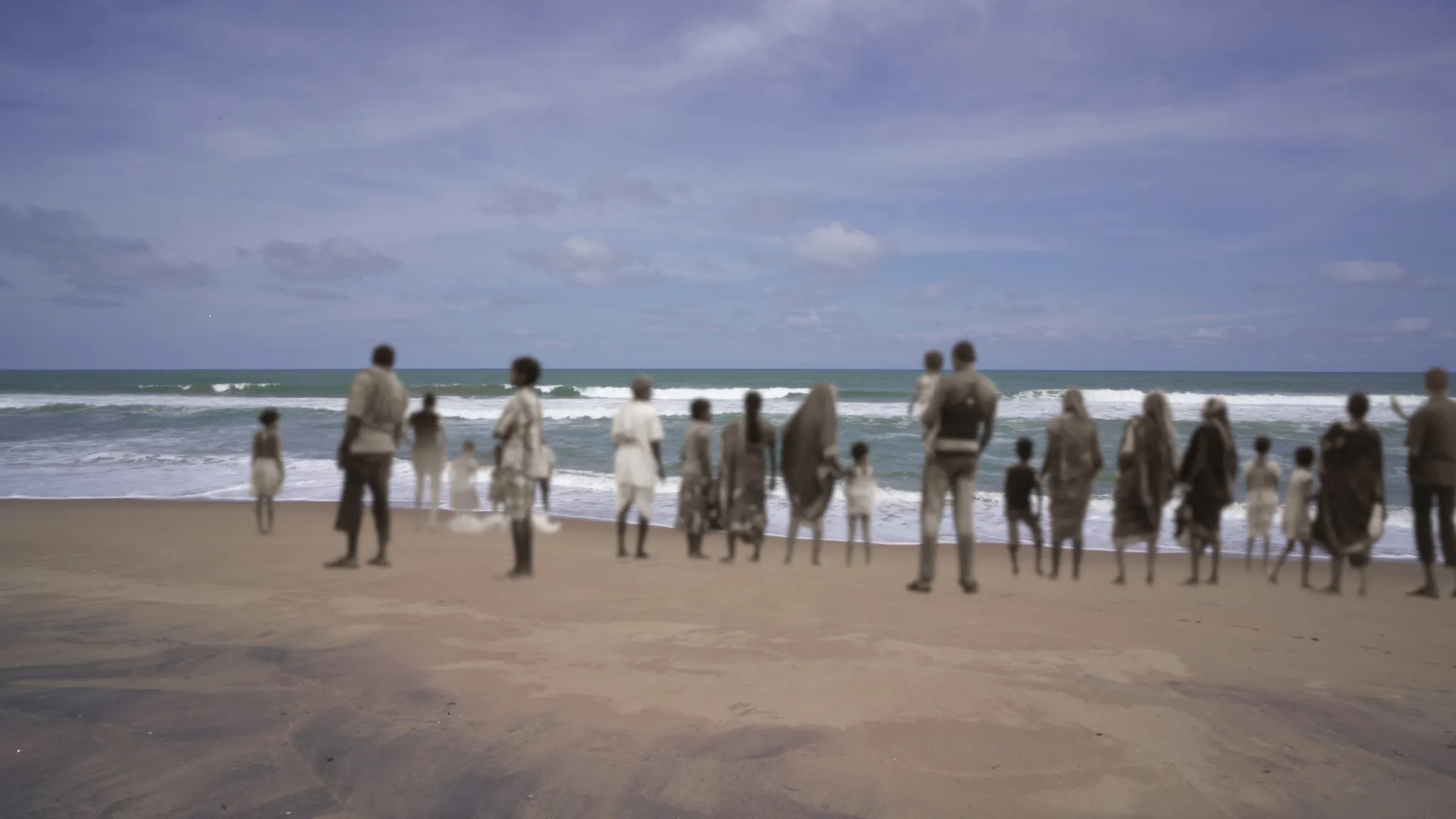 A still from the film, Rice Hunger Sorrow. A group of people standing on the sand, looking over at the waves of the Chilika Lake.