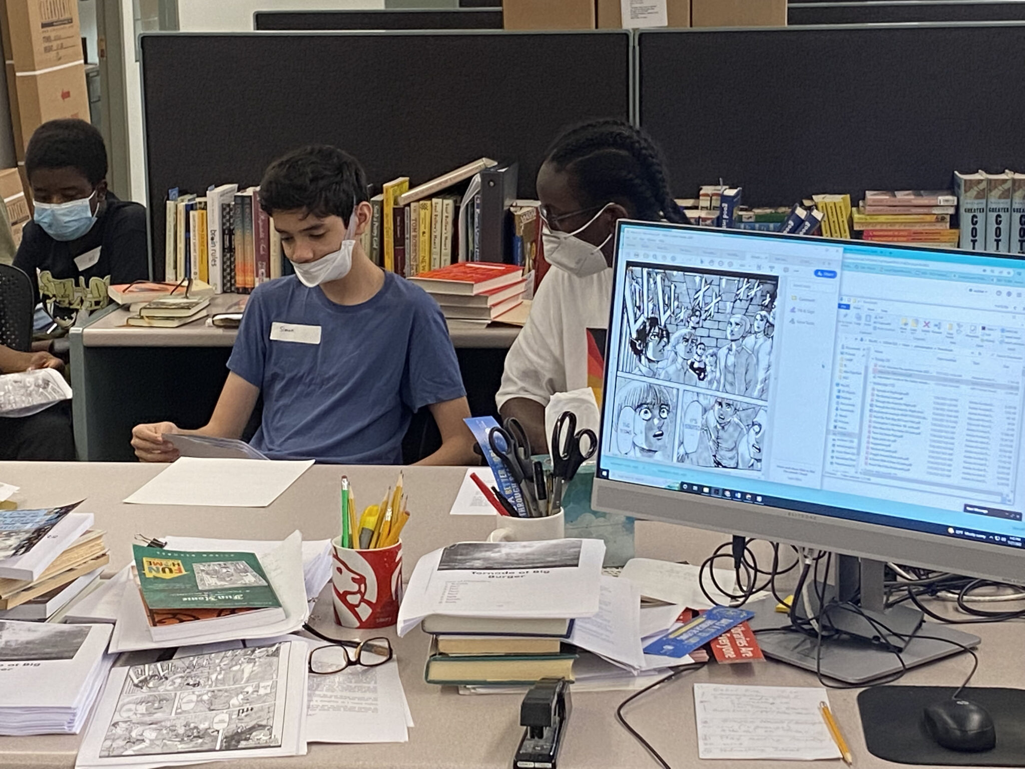 Three students are seated in front of a desk with a monitor with a white and black graphical sketch of a storyboard scene, as they learn how to make audiobooks at the Andrew Heiskell Braille and Talking Book Library.