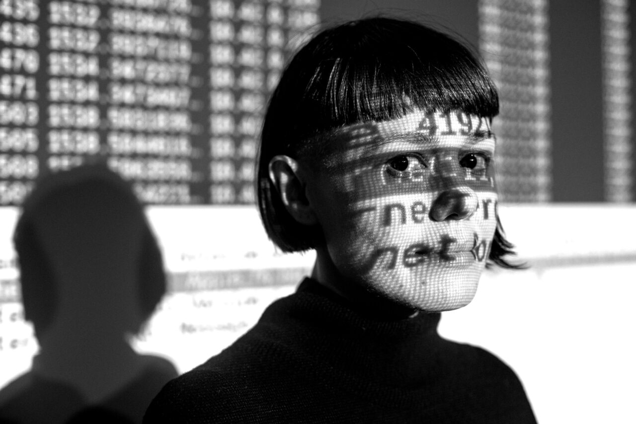 Woman with short hair and bangs with graphical wireless network data projected behind her head and on top of her face.